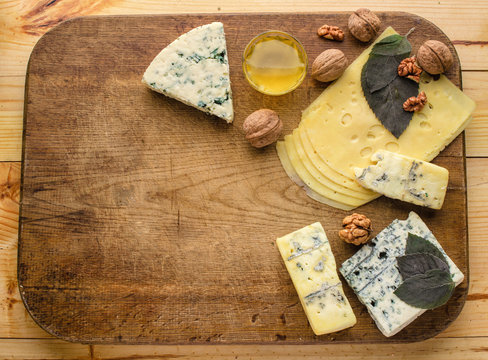Assortment of cheese with honey, nuts and grape on a rustic cutting board wooden background