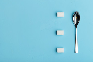 Spoon and sugar cubes on blue background, the view from the top with place for your text. Conceptual food photos