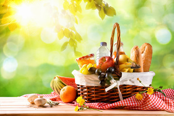 Picnic wicker basket with food on table in the field