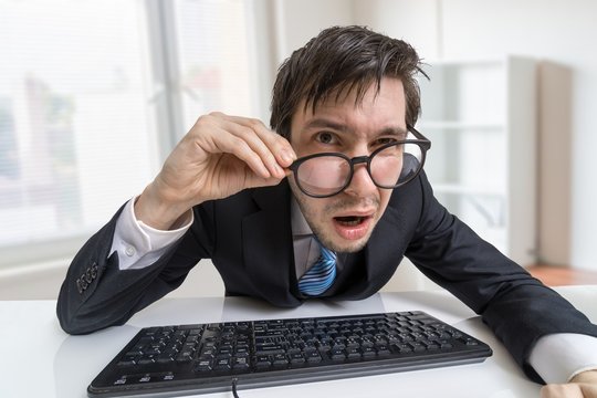 Confused or unsure man is working with computer and looking at you.