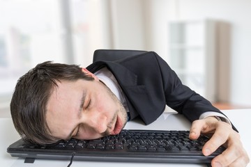 Exhausted or tired businessman is sleeping on keyboard in office.