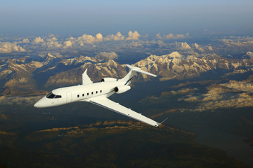 Business jet airplane flying over mountains.