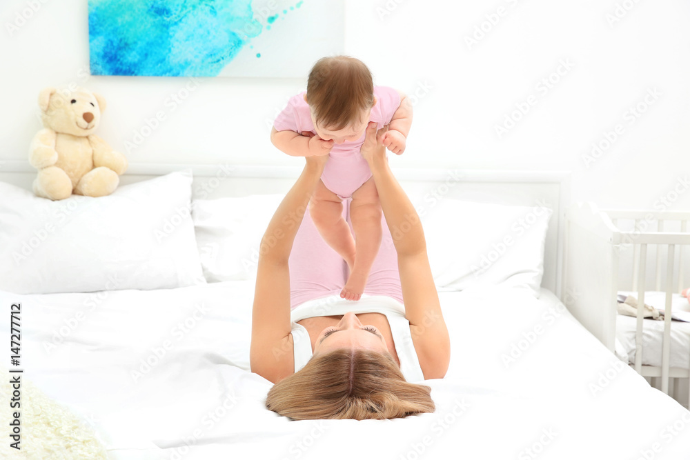 Poster Young mother playing with her baby on bed