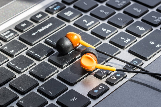 Close up picture of orange earphones on laptop. Technology concept