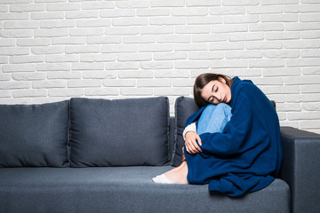 Sad depressed woman at home sitting on the couch, looking down and touching her forehead, loneliness and pain concept