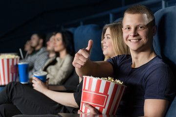 Handsome young man showing thumbs up enjoying a movie at the cinema
