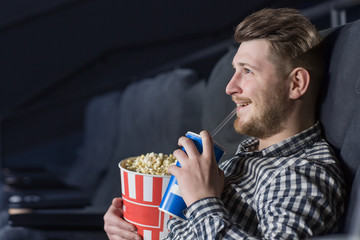 Young cheerful handsome guy enjoying a movie at the cinema
