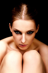Young nude woman with dark eye make up sitting on the floor