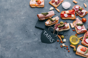 Still life, food and drink, holidays concept. Assortment of spanish tapas or italian antipasti, jamon, prosciutto, chorizo, salami on a grunge black board, rustic style.
