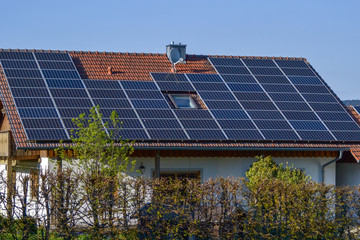 Solar panel on a red roof reflecting the sun and the cloudless blue sky