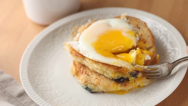 Senior man cuts into pancakes topped with a fried egg