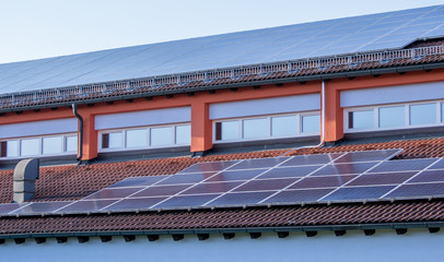 Solar panel on a red roof reflecting the sun and the cloudless blue sky