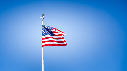 American flag waving on a pole with eagle ornament on the top. Blue sky vignette. For Memorial Day, Veterans Day, July 4, Independence Day or other patriotic occasion. Copy space