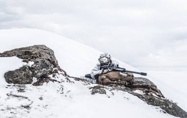 Army soldier with Sniper rifle in action in the Arctic. He lies among the cold rocks and stones,...