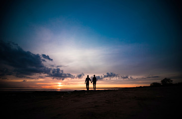 Silhouettes of woman and man on a background of colorful sunset of a cloudy day on the beach