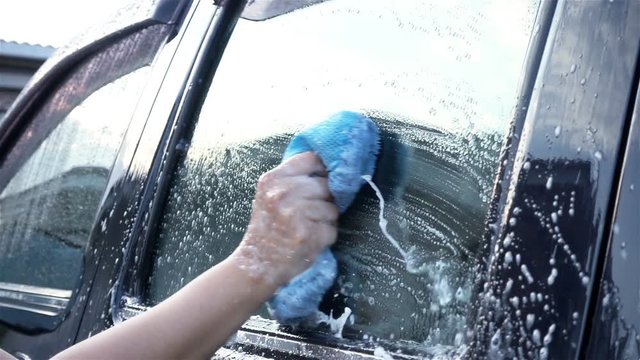 Slow motion, close up woman's hand cleaning car with blue sponge