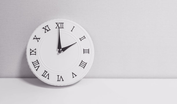 Closeup white clock for decorate in 2 o'clock on white wood desk and wallpaper textured background in black and white tone with copy space