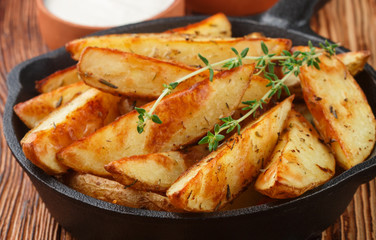 Potato wedges with garlic, spices and thyme in a cast iron skillet. Ketchup and white sauce. Selective focus