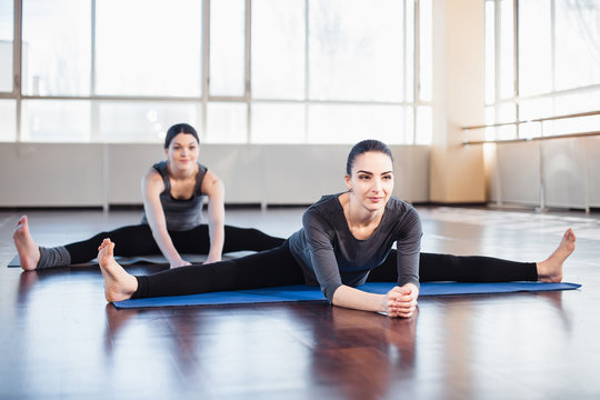 Two young women doing stretching out in the fitness room