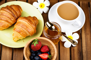 Cup of coffee and croissants on wooden background.