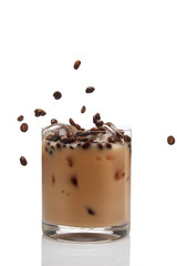 Coffee beans falling into cocktail with Irish creme liqueur in a glass full of ice.