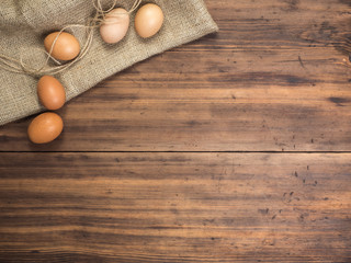 Brown chicken eggs lay on a piece of burlap on a wooden table from the old boards. Top view. Three fresh chicken eggs close-up, background for advertising or Easter greetings, rustic style
