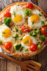 hearty breakfast of pizza with eggs, broccoli, tomatoes closeup on the table. Vertical top view