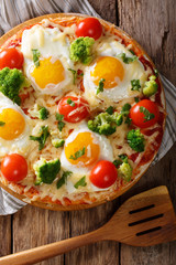 Pizza with eggs, cheese, broccoli, tomatoes and herbs close-up. Vertical top view