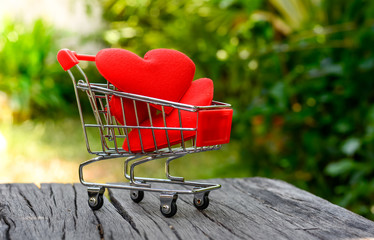 red heart  in mini shopping cart on wooden over blurred green light bokeh background. Image for happy valentine day concept.