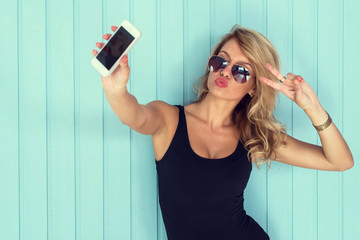 blonde woman in bodysuit with perfect body taking selfie smartphone toned instagram filter