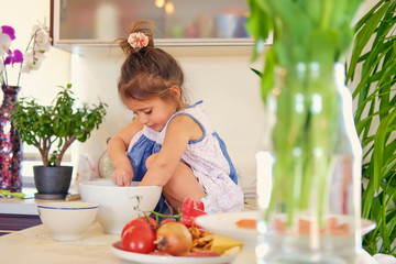 A cute little girl sits on a table and trying to cook.