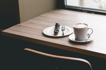 Cup of coffee on wooden table with eclair