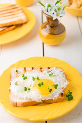 Toast with egg in yellow plate near vase with flower on white wooden background. Healthy breakfast.