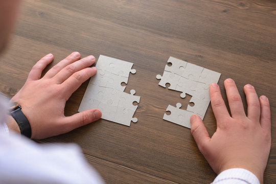 Male hands on a wooden office desk pick puzzle. Macro with blur and soft focus