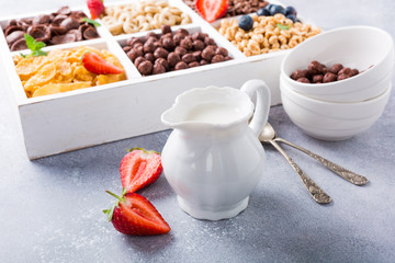 Milk jug and variety of cold quick breakfast cereals with berries in white wooden box, healthy eating concept, selective focus.
