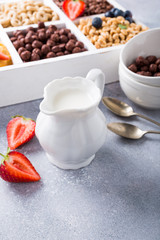 Milk jug and variety of cold quick breakfast cereals with berries in white wooden box, healthy eating concept, selective focus, copy space.