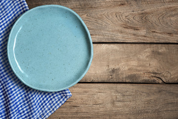 Top view of blank dish and blue tablecloth on a wood background with copy space.