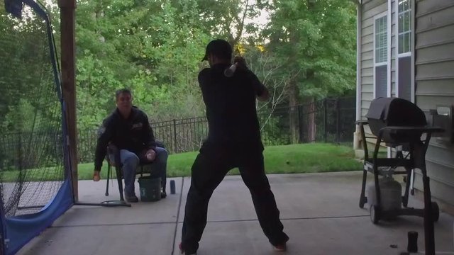Slow motion of two men practicing hitting a baseball on a net