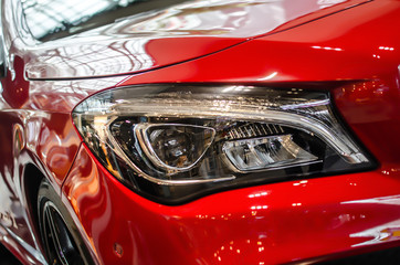 The headlamp of a red sports car of aggressive form with a part of the hood and black wheel, bumper and partronik