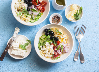 Mediterranean pasta salad. Pasta  farfalle, tomatoes, cucumbers, olives, feta cheese and arugula salad. On a blue background, top view. Flat lay