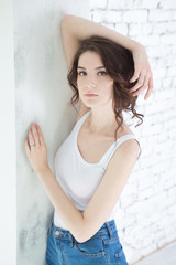 Beautiful  Woman the young woman in a white undershirt and jeans is looking at camera    while standing  against white brick wall