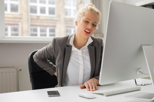 Woman with back pain sitting by the computer at the office
