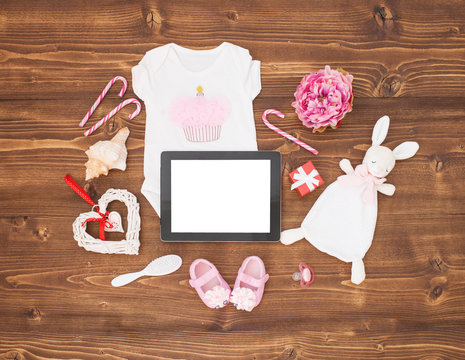 Tablet computer and baby girls clothes on wooden background