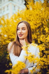 Portrait of woman standing near yellow flowers tree in garden.