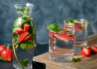 Detox water with fresh mint and strawberries in transparent glasses against the blue wall