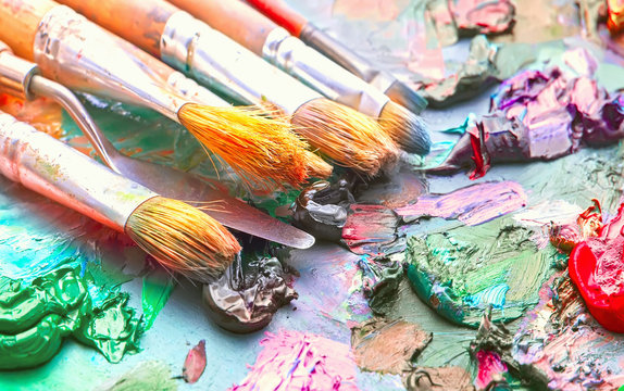 used brushes in an artist's palette of colorful oil paint for drawing