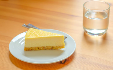 Cheese cake on white disk and aglss of water.