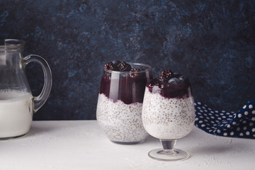 Organic chia pudding in two glasses with coconut milk and blackberry smoothie on top. Dark rustic...