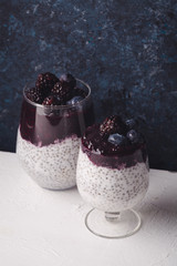 Organic chia pudding in two glasses with coconut milk and blackberry smoothie on top. Dark rustic...