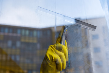 Scraper for washing windows in hands in yellow gloves. Wash the dirty and dusty windows in the...